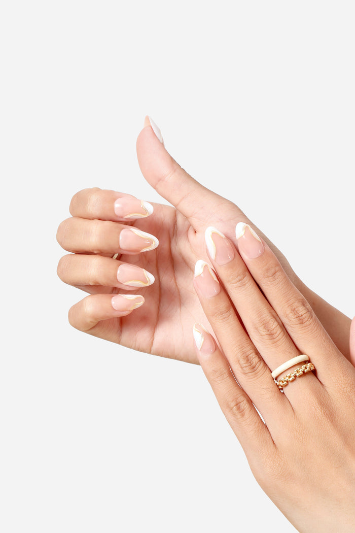 Short almond press-on nails with a nude base and a unique gold and white wavy French tip design.
