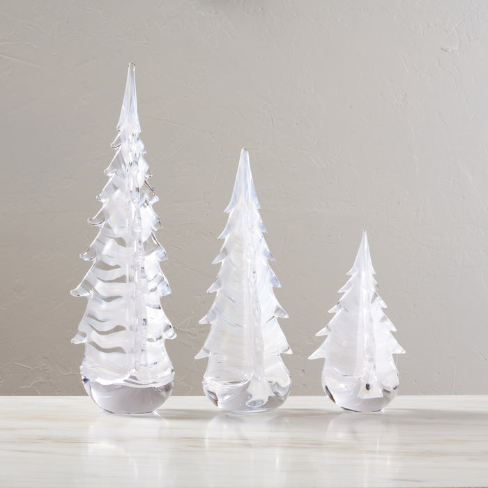 Three clear glass evergreen tree figurines in graduated sizes with frosted white details on a white surface.