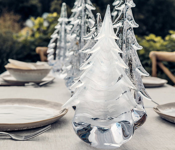 Clear glass evergreen tree figurine with frosted textured surface on white tablecloth with place settings.