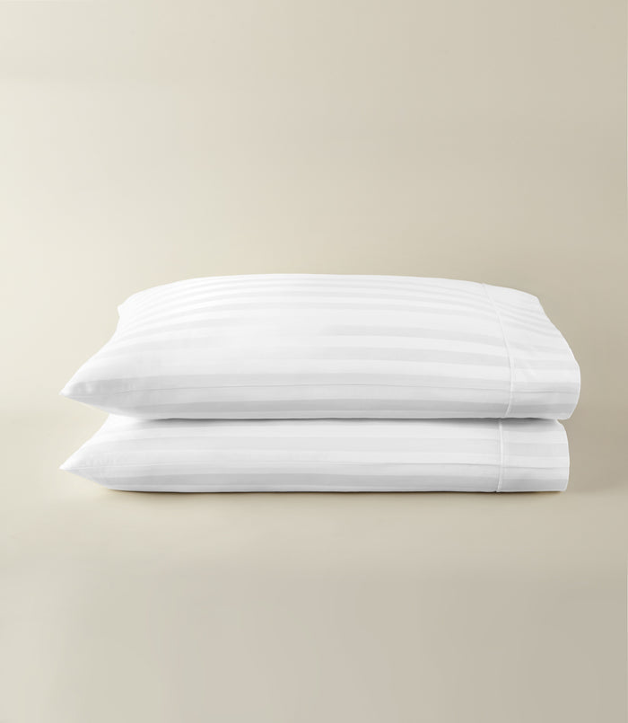 Soprano Stripe Sateen Pillowcases stacked on a beige background, White