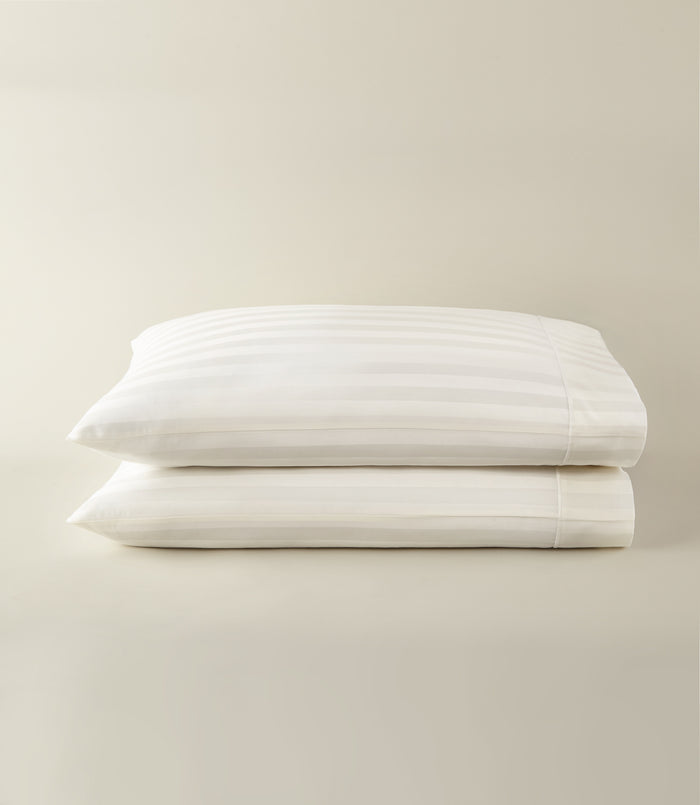 Soprano Stripe Sateen Pillowcases stacked on a beige background, Ivory