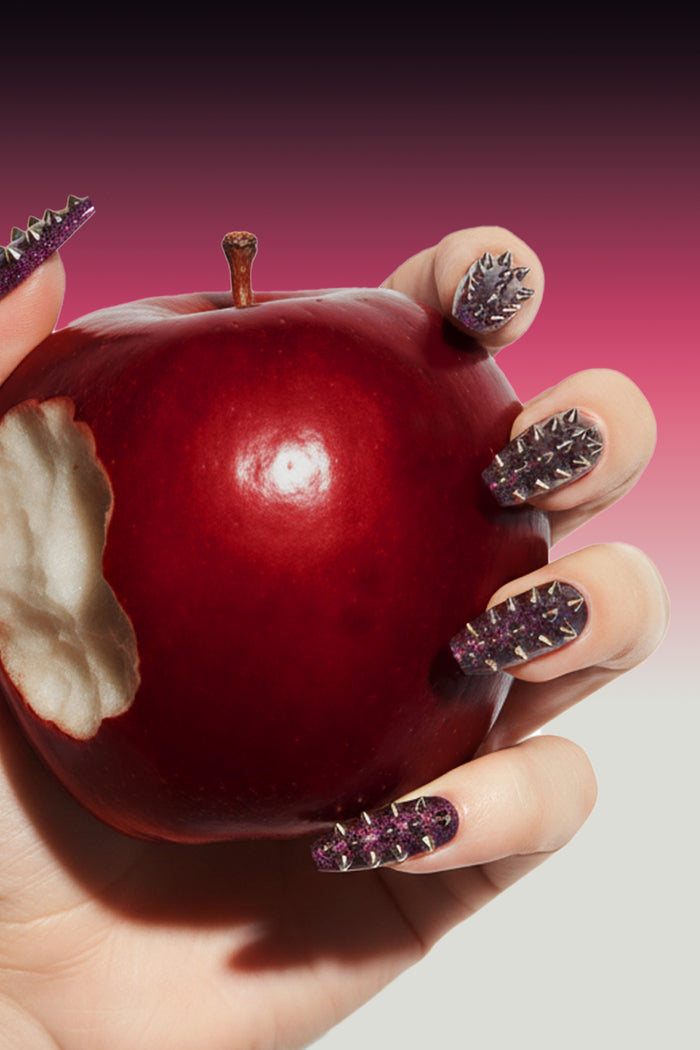 Coffin press-on nails with spikes and glitter holding a bitten red apple.