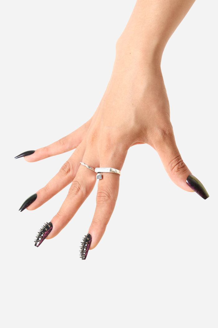 Hand showcasing spiked coffin press-on nails in deep wine tones with glitter and silver studs, wearing a unique silver ring.