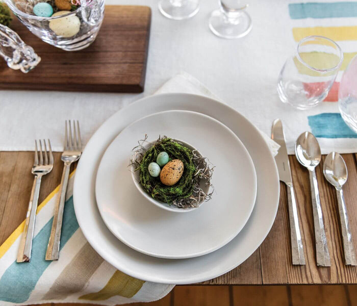 Linen table runner with horizontal stripes in blue, yellow, and pink on a wood dining table.