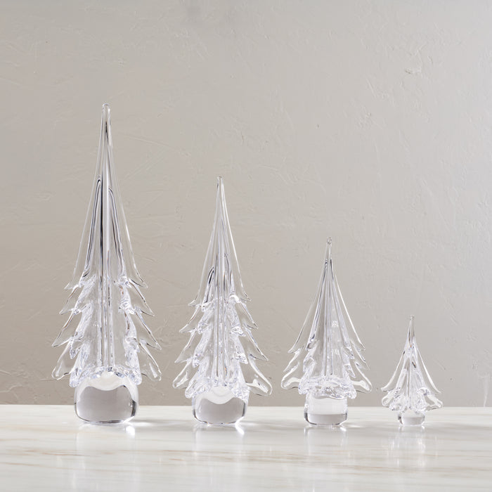 Four clear glass evergreen tree-shaped decorations in decreasing sizes with white frosted bases.