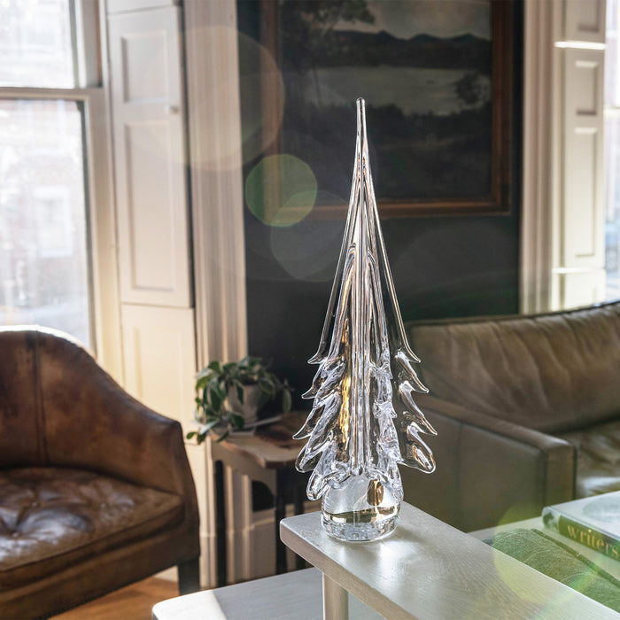 Clear glass evergreen tree figurine with layered branches on a white base, displayed on a table.