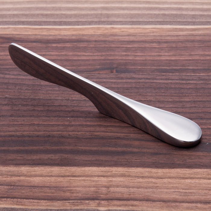 Silver-toned stainless steel butter knife with curved handle, displayed on a wooden surface.