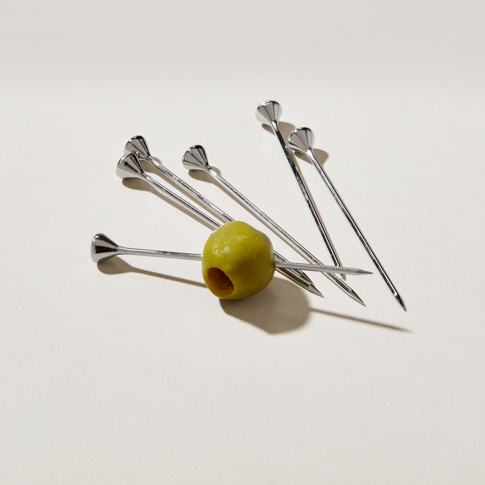 Six stainless steel cocktail picks with decorative fan-shaped tops, one holding a green olive.