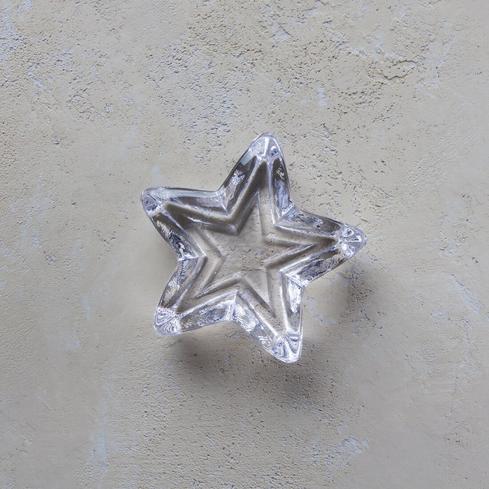 Small clear glass star-shaped paperweight with five points on textured surface.