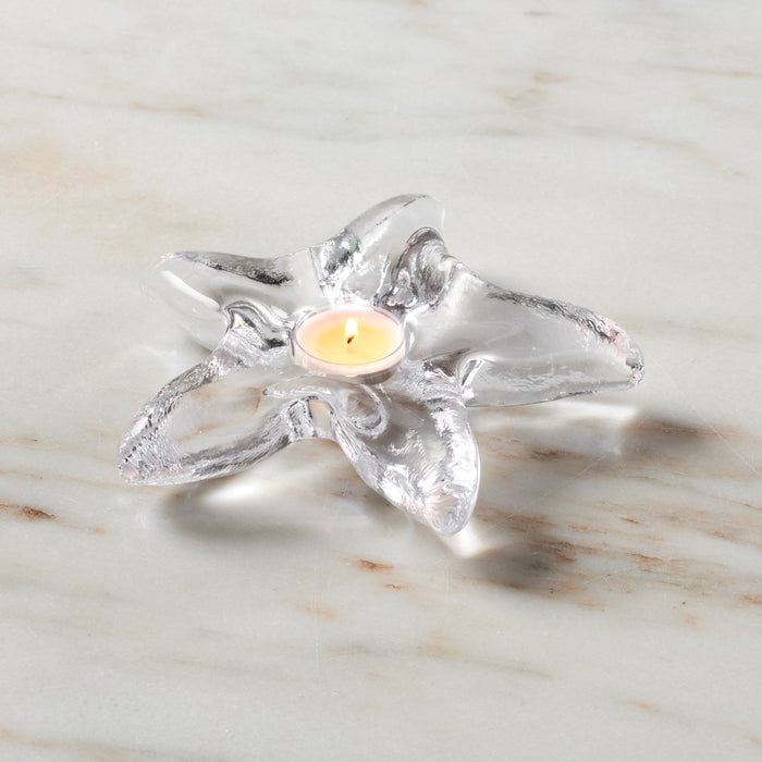 Clear glass starfish-shaped tealight holder with lit cream candle in center on marble surface.