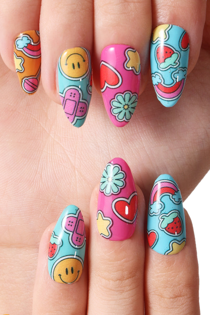 Press-on nails featuring fun, cartoonish designs like smiley faces, band-aids, strawberries, and rainbows in vibrant colors.