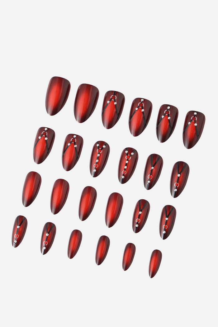 Set of almond-shaped press-on nails with a gradient of deep red to black, adorned with black straps and silver rhinestones.