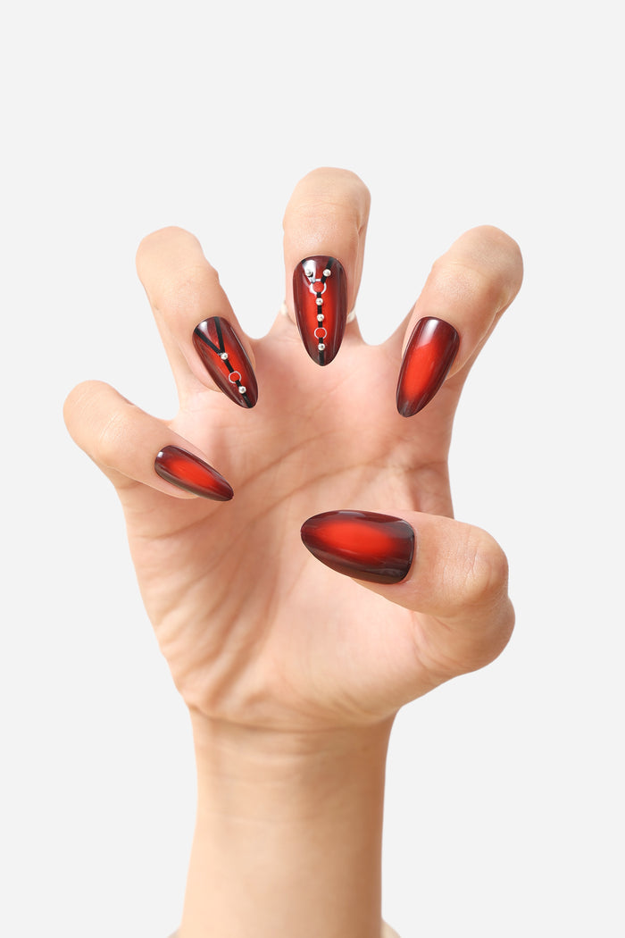 Almond press-on nails with glossy crimson gradient and black accents, adorned with small silver studs.