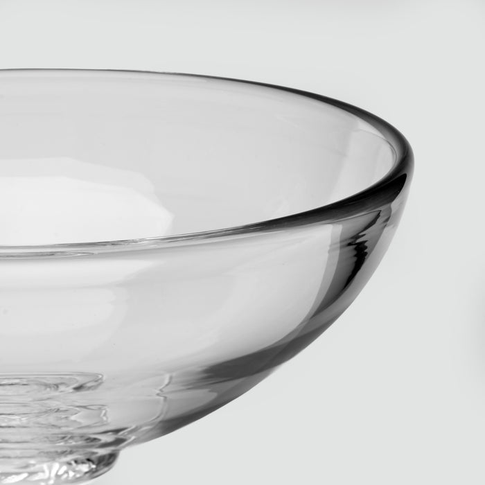 Close-up of a clear glass bowl with a thick rim and pedestal base, photographed against a light gray background.