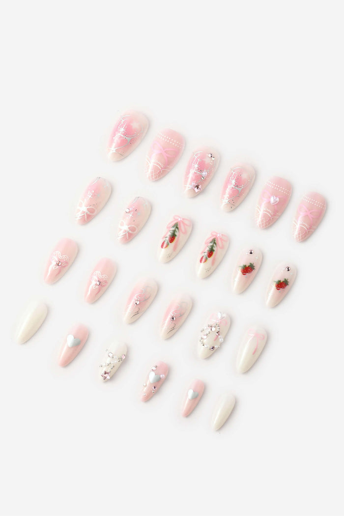 Pink and white almond press-on nails with strawberry, heart, and bow designs.