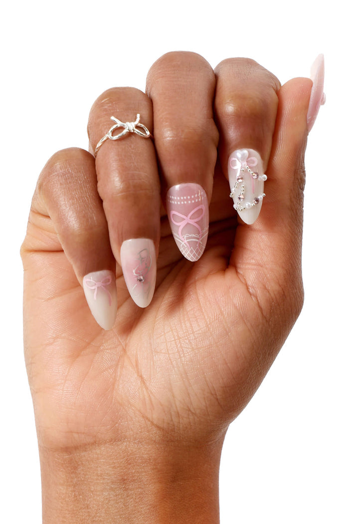 Almond press-on nails with pink bows and pearl accents, on a hand wearing a silver bow ring.
