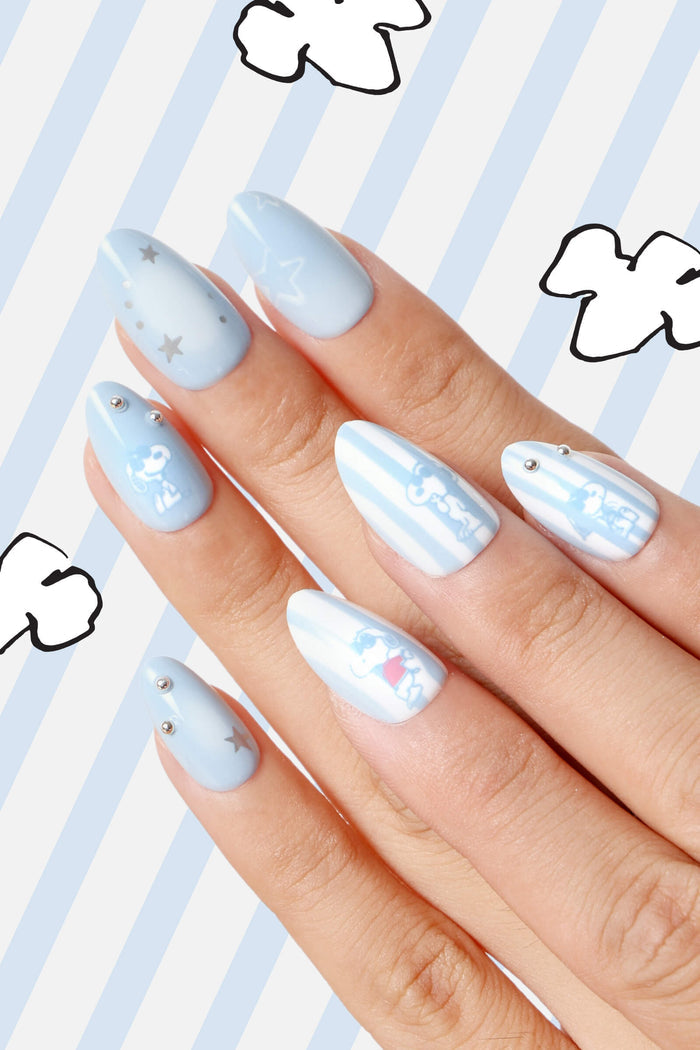 Short almond press-on nails with light blue base, featuring Snoopy characters, stars, and subtle silver embellishments.