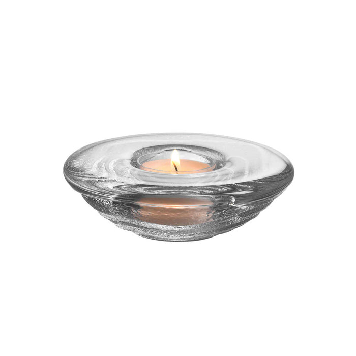 Clear glass tealight holder with lit tealight candle in center well.