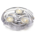 Three lit tealights in cream-colored cups set in a silver textured circular holder.