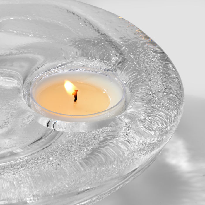 Lit cream-colored tealight candle nested in a textured clear glass holder with marbled pattern.