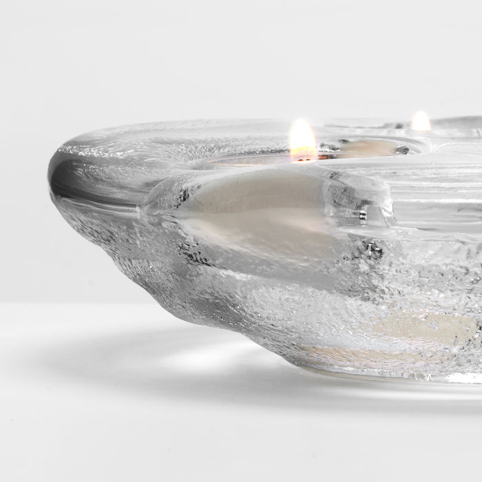 Clear glass tealight holder with lit tealight candle inside and textured surface detail.