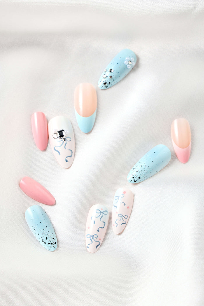 Pastel almond press-on nails with bows, glitter, and gem accents on white satin.