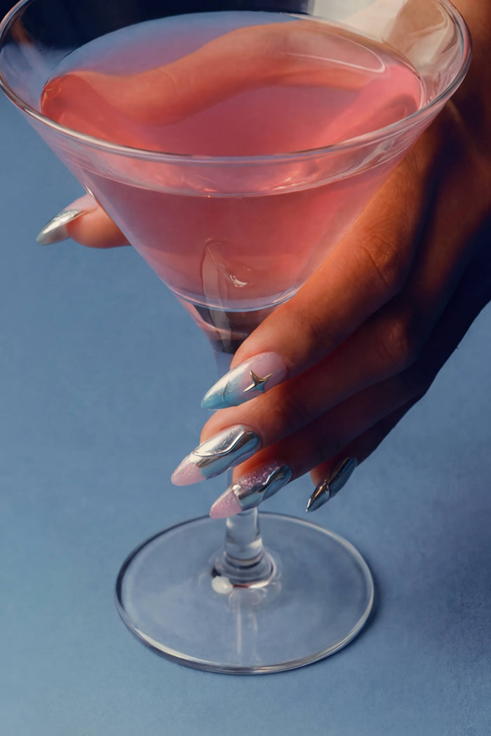 Press-on nail with metallic silver, blue, and pink design, holding a cocktail glass.