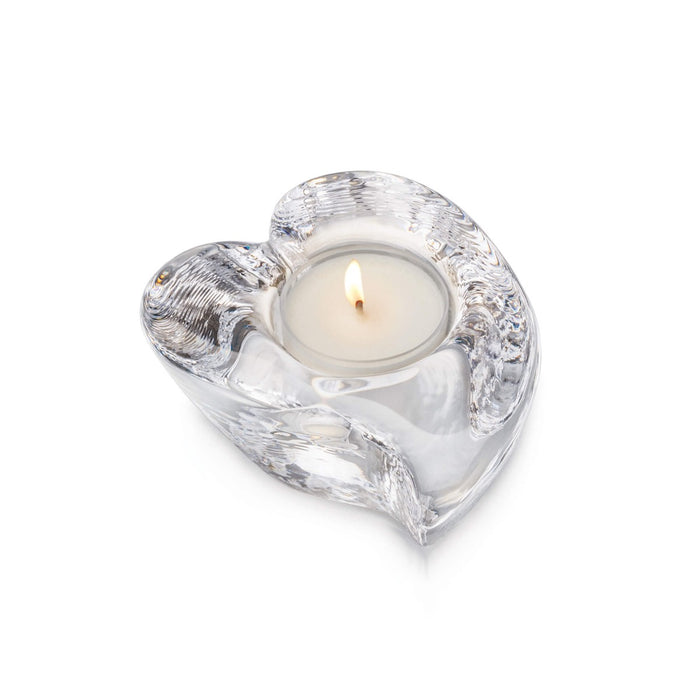 Clear glass heart-shaped tealight holder with lit cream candle inside.