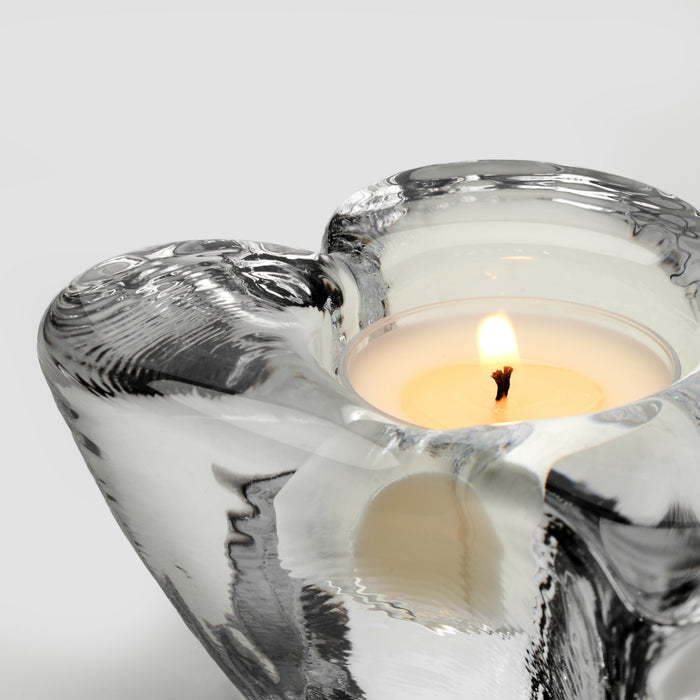 Heart-shaped tealight holder with twisted silver and white design, containing a lit cream candle with flame.