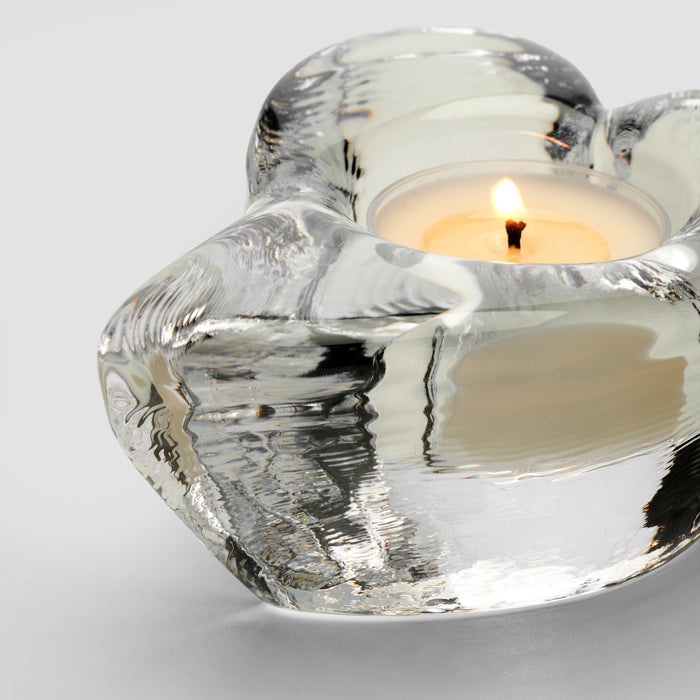 Clear glass heart-shaped tealight holder with twisted design and lit candle inside.