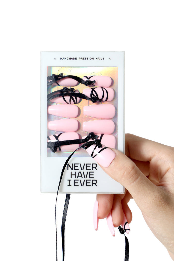 Pink coffin press-on nails with black ribbon accents from the Wǎn 绾 (tie/bind) collection by Dawang, held by a hand.