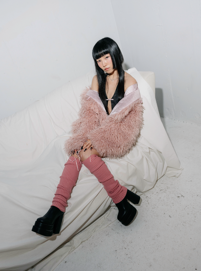 Woman in pink leg warmers, black platform boots, and fluffy pink jacket.
