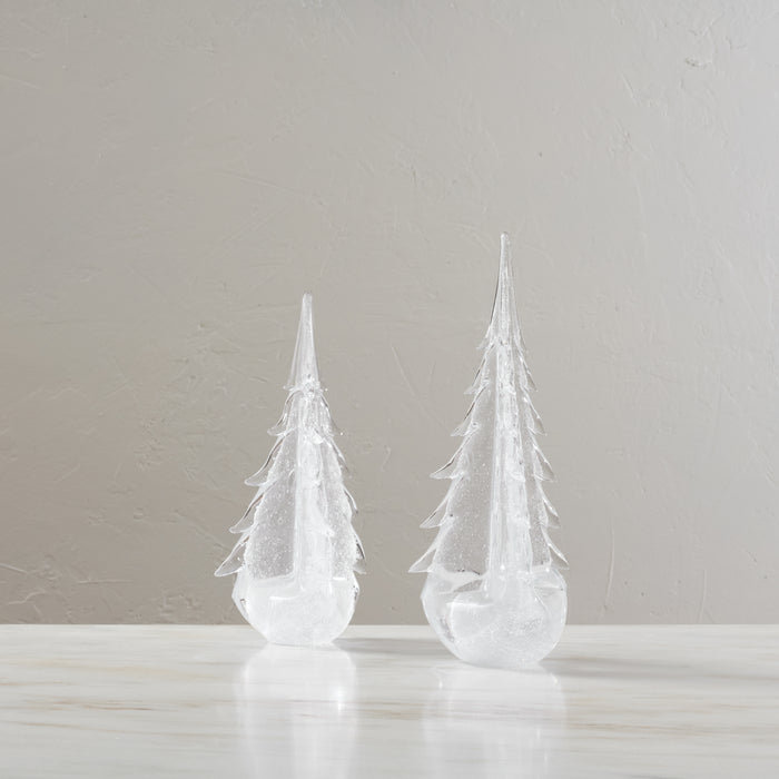 Two white frosted glass evergreen tree-shaped candles with pointed tops and tiered branches on a light surface.