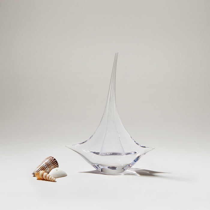Clear glass sailboat with pointed sail and rounded base, displayed with small decorative shells.
