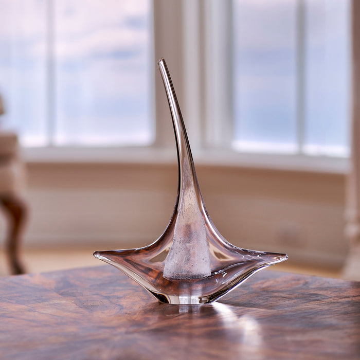 Glass sailboat sculpture with curved sail and tapered mast on wooden surface.