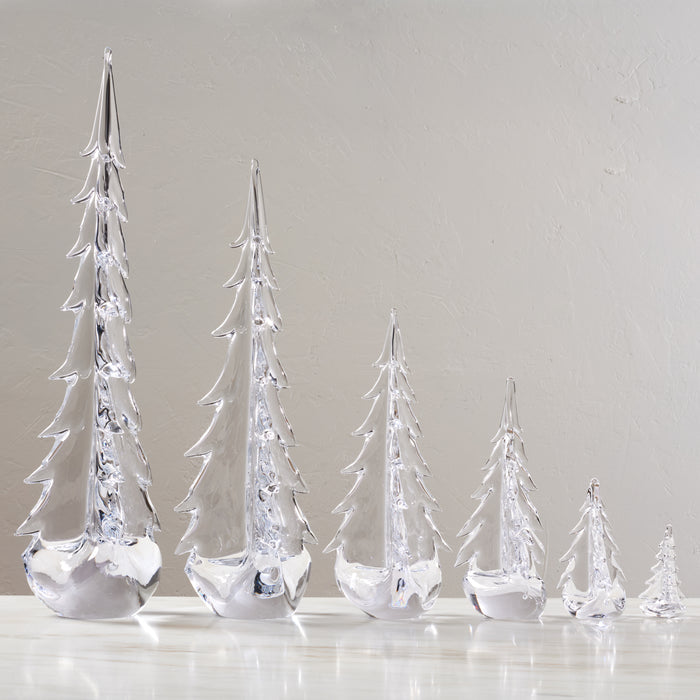 Five clear glass evergreen trees in graduating sizes with white frosted bases.