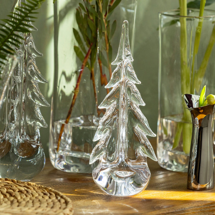 Clear glass evergreen tree figurine with layered branches and pointed top on wooden surface.