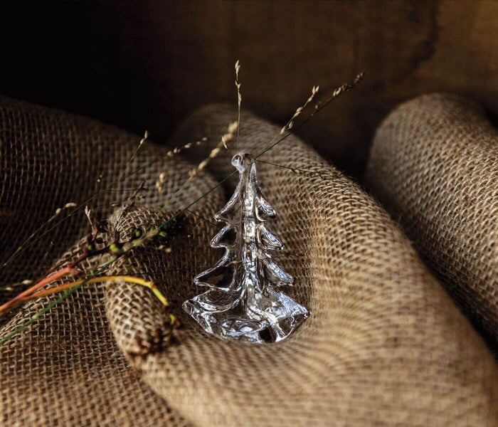 Silver evergreen tree ornament with textured branches displayed on natural burlap fabric.