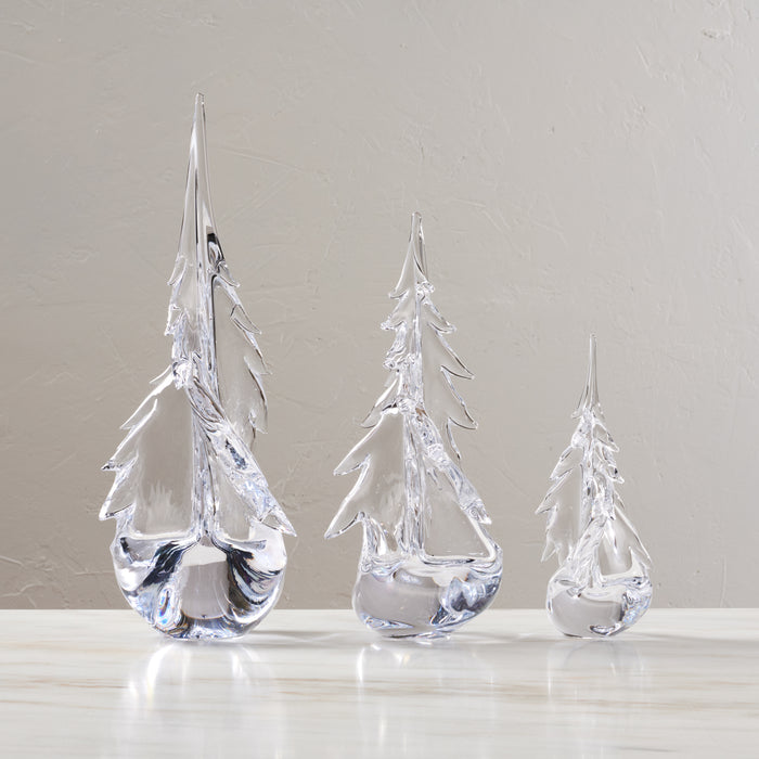 Three clear glass evergreen tree figurines in graduated sizes with pointed tops and detailed branch texture.