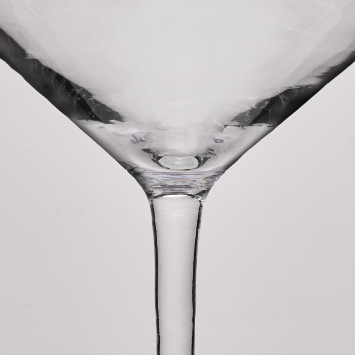 Close-up of a clear glass martini glass showing the base and stem against a light gray background.