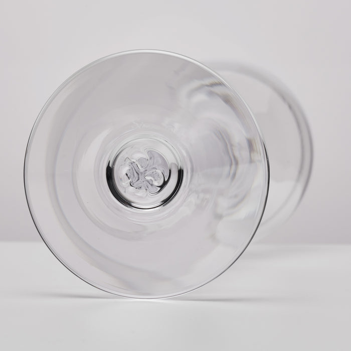 A clear glass coupe glass shown from a bottom angle, highlighting its circular bowl and stem base, set against a clean white background.