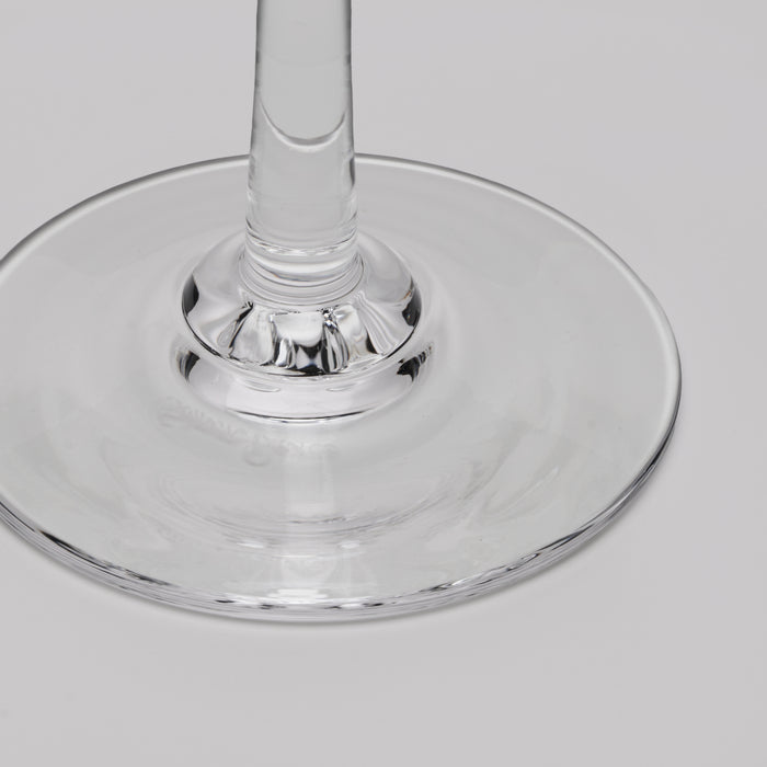 A close-up of a clear glass wine glass base and stem on a light gray background.