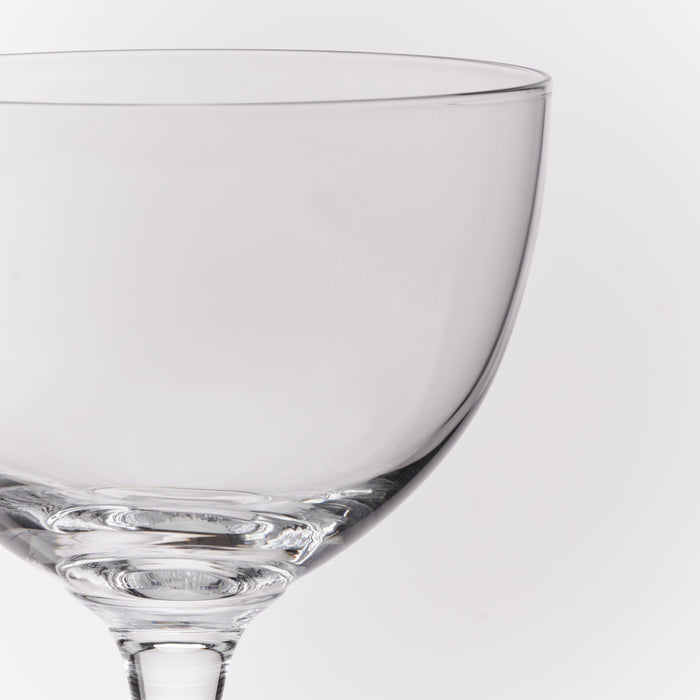 A close-up of a clear glass coupe glass on a light gray background.