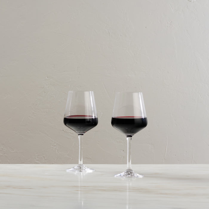 Two wine glasses filled with red wine on a white surface against a light textured wall.