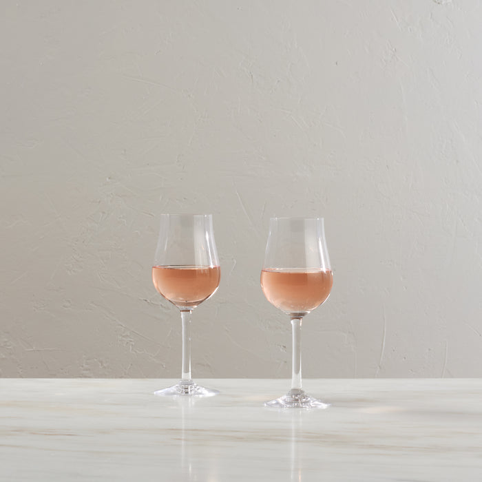 Two tulip-shaped wine glasses filled with rosé wine on a white surface against a textured gray wall.