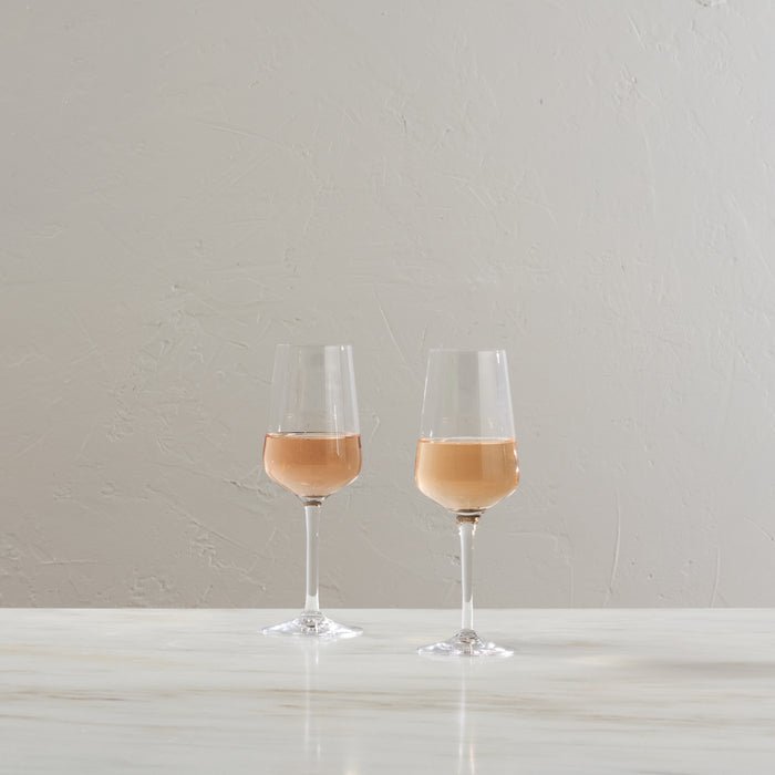 Two glasses filled with pale rosé or white wine on a white surface against a neutral background.