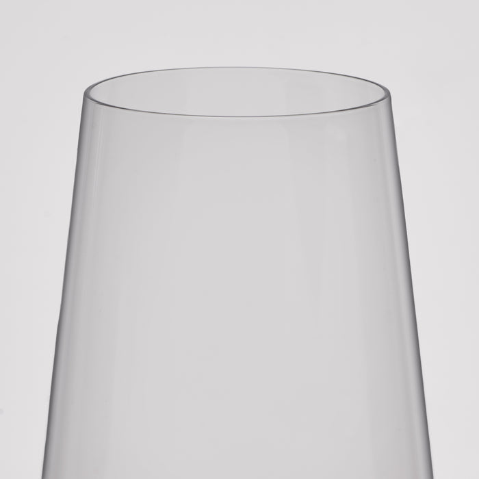 A close-up of a clear wine glass with a flared, tapered rim, shown against a plain light gray background.