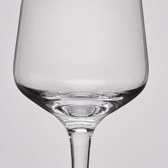 A close-up studio shot of a clear glass wine glass against a light gray background.