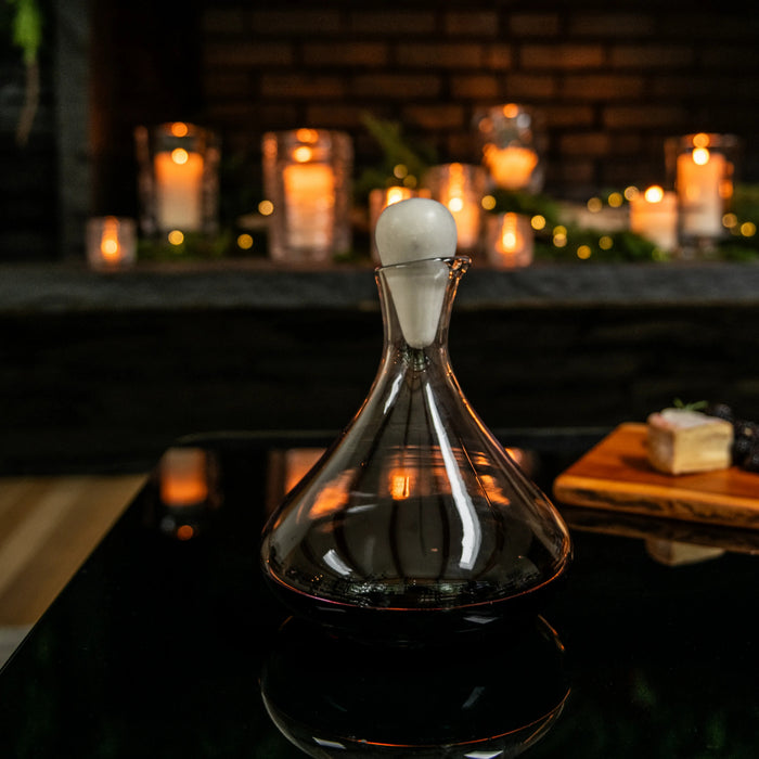 Clear glass wine decanter with white marble spherical stopper, filled with dark red wine.