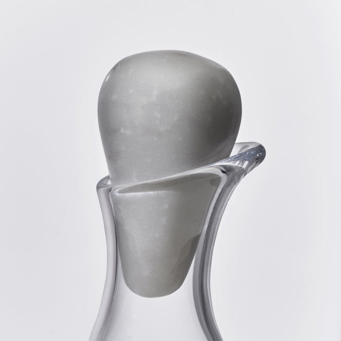 Clear glass wine decanter with curved body and marble sphere stopper on top.